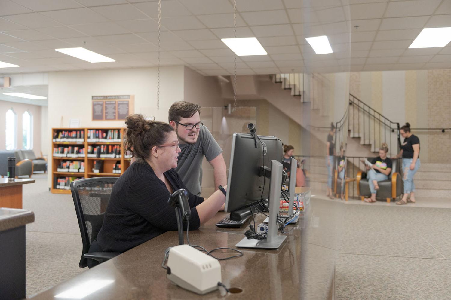 A staff member and student review a database at the King Library